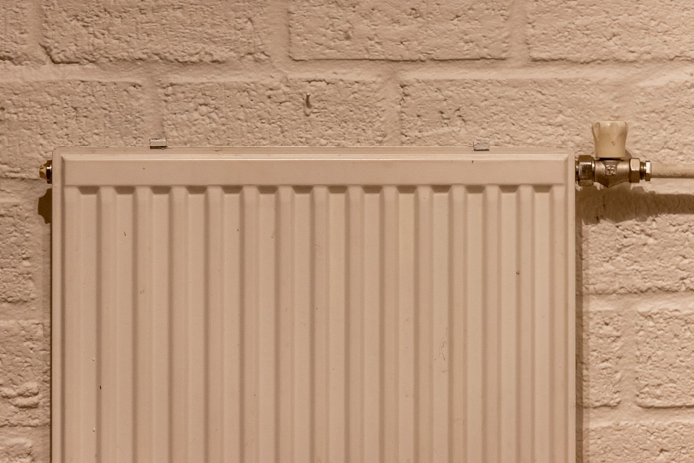 A white panel radiator with a valve, mounted on a painted brick wall.